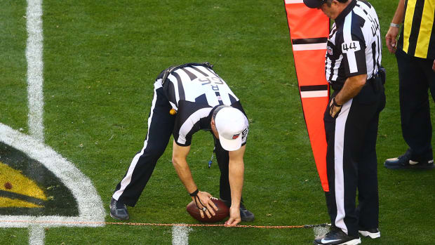 A ref leans down to place a football at an exact spot on a first-down chain
